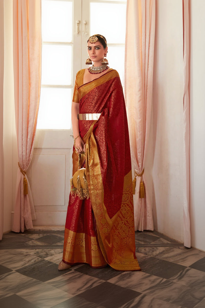 Woman in a red and gold saree standing in a room with pink curtains.