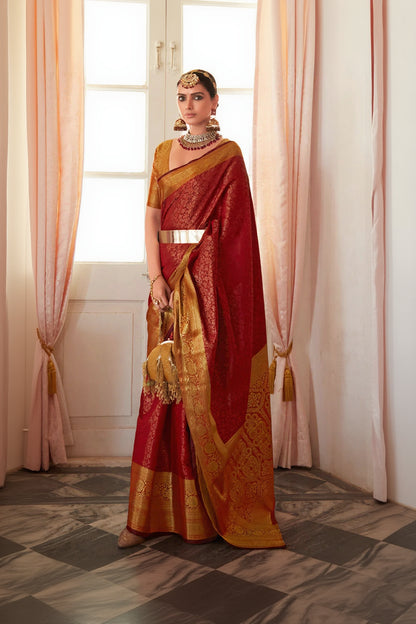Woman in a red and gold saree standing in a room with pink curtains.