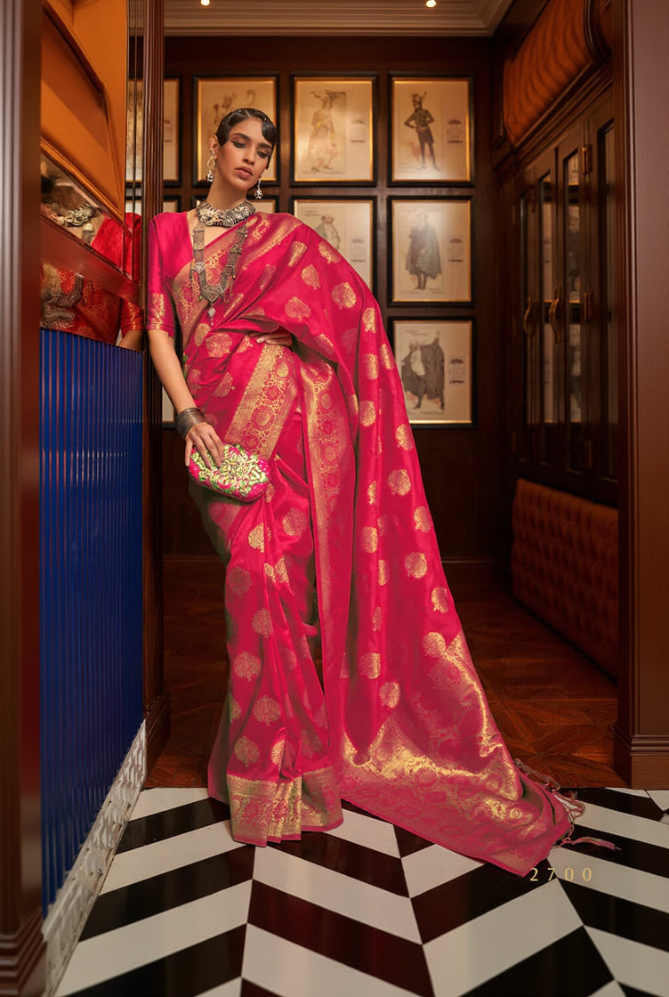 Woman in a red saree with gold patterns standing in a room with framed pictures on the wall.
