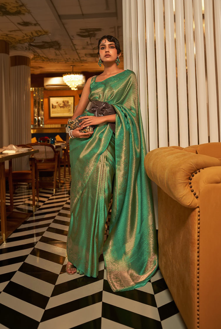 Woman in a green saree standing in a room with a checkered floor and a couch.