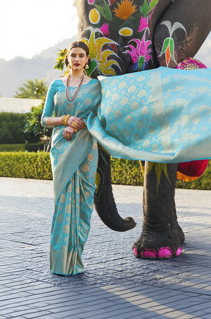 Woman in a light blue saree standing next to an elephant with colorful decorations.